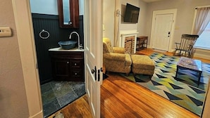 Quarto com piso de madeira, lareira, televisão e uma cadeira de balanço.