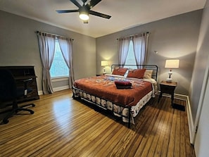 A bedroom with a bed, two bedside tables with lamps, a ceiling fan, and a desk.