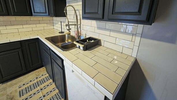 Uma cozinha com armários escuros, uma pia de aço inoxidável e um painel de azulejos.