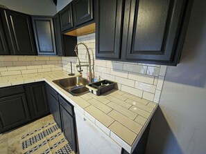 A kitchen with dark cabinets, a stainless steel sink, and a tiled backsplash.