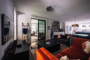 A modern living room with a sofa, coffee table, and TV. -  5 Min Walk to Beach + Game Room + Wood & Propane Fire Pits - Heatonelli Haven (South Haven)