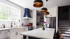 A modern kitchen with white cabinets, a central island, and pendant lighting. -  5 Min Walk to Beach + Game Room + Wood & Propane Fire Pits - Heatonelli Haven (South Haven)