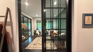 A room with a large sliding glass door, a wicker chair, a sofa, and a patterned rug. -  5 Min Walk to Beach + Game Room + Wood & Propane Fire Pits - Heatonelli Haven (South Haven)
