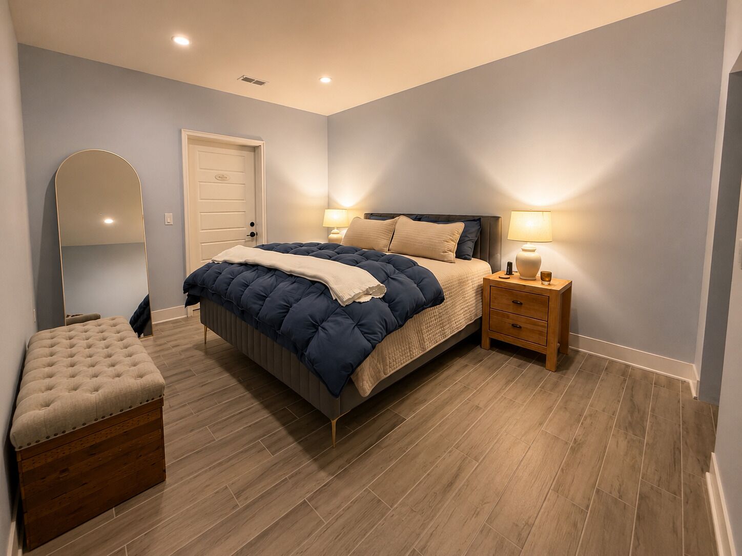 A bedroom with a bed, bedside tables, a bench, a mirror, and a door.