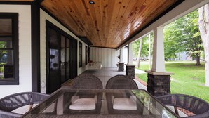 A covered outdoor seating area with wicker chairs and a glass table, a stone fireplace, and a view of a grassy yard. -  5 Min Walk to Beach + Game Room + Wood & Propane Fire Pits - Heatonelli Haven (South Haven)