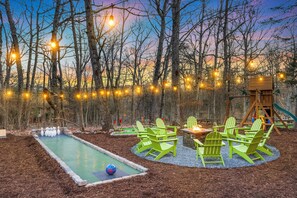Un jardin avec une table de billard, des fauteuils Adirondack verts et une structure de jeu en bois.