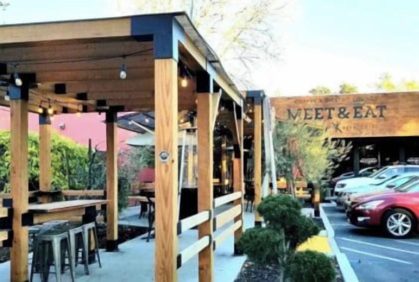 An outdoor seating area with tables and chairs, a covered structure, and a building with 'VEET & EAT' signage.