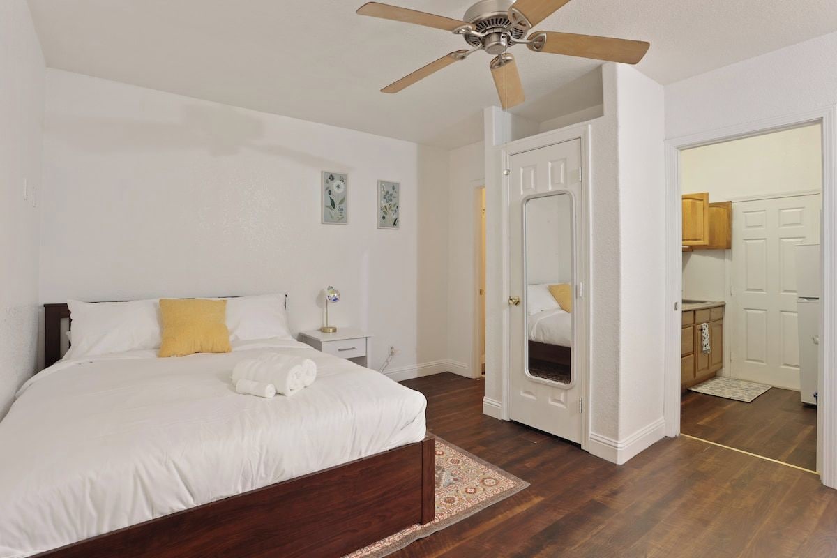 A bedroom with a bed, a ceiling fan, a nightstand, and a door leading to a bathroom.