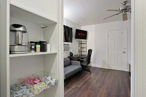 A room with a kitchenette, a gray sofa, a black office chair, a TV mounted on the wall, and a ceiling fan. - Prime 2BR Upstairs Unit in the heart of Sacramento (Sacramento)