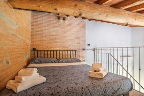 A bedroom with a brick wall, a bed with a patterned bedspread, and a balcony with a metal railing. - Uffizi Suite II in Florence-hosted by Sweetstay (Florence)