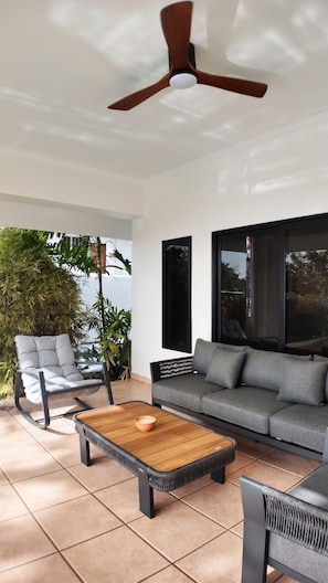 A modern living room with a ceiling fan, a grey sofa, a wooden coffee table, and a black chair. - Luxury 7-bedroom villa with Ocean Views & Pool in Mt. Irvine (Mt. Irvine)