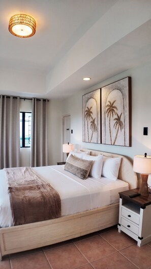 Une chambre d’hôtel comprenant un lit, des tables de chevet, des lampes, une fenêtre avec des rideaux et des œuvres d’art murales.