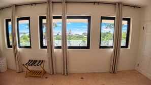 A room with three windows, a view of greenery and a building, and a wooden chair.