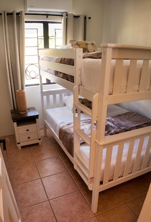 A bunk bed room with a window, curtains, a bedside table, and a lamp. - Luxury 7-bedroom villa with Ocean Views & Pool in Mt. Irvine (Mt. Irvine)