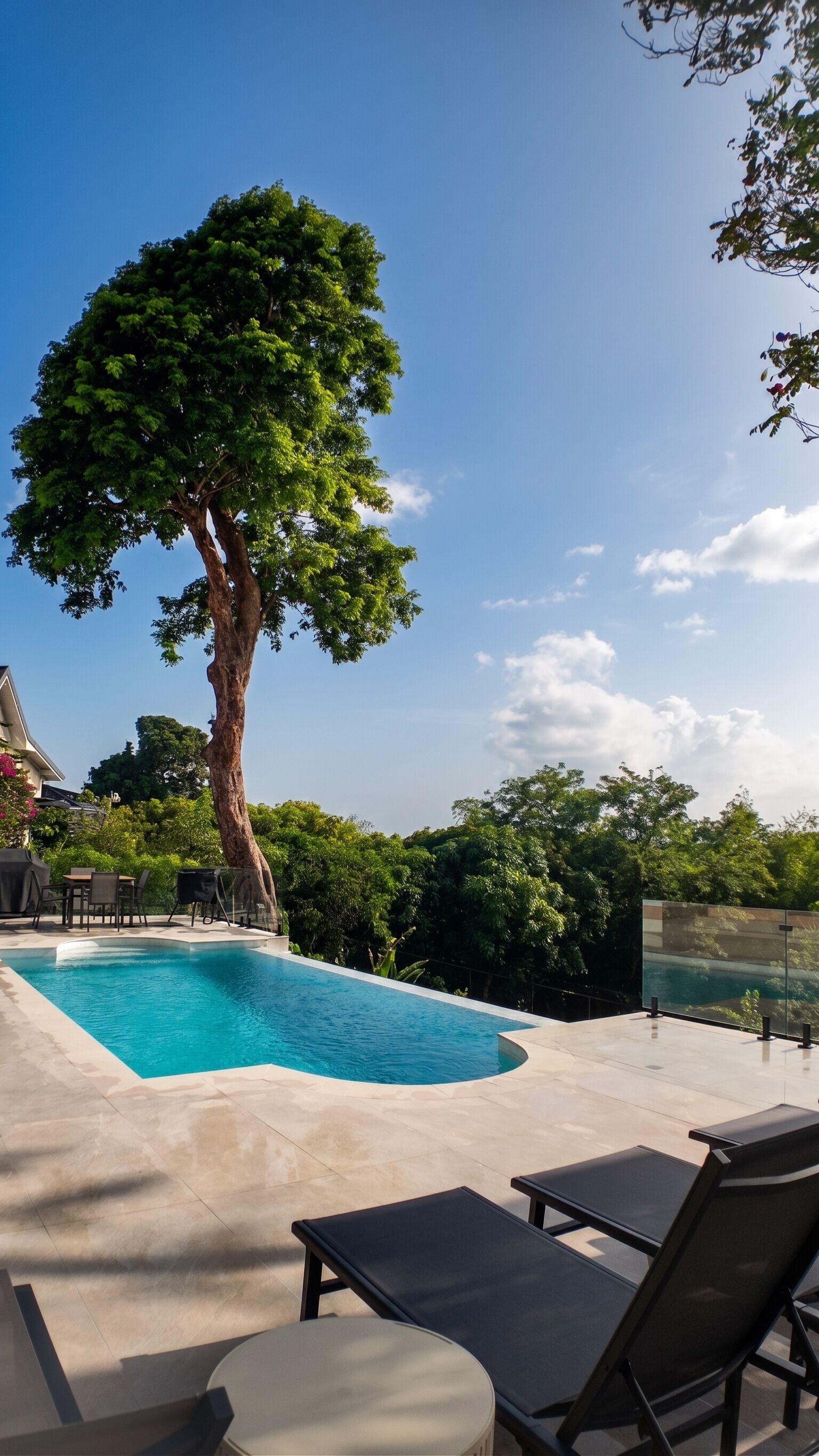 A swimming pool with a tree in the center, surrounded by lounge chairs and a clear sky.