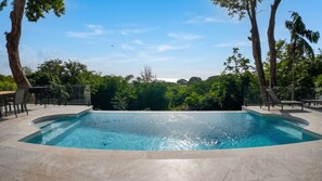 Une piscine à bord incurvé, entourée d’un patio aménagé avec des chaises et des tables.