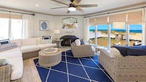 A living room with a large window, a ceiling fan, and a view of the beach. - Seas the Moment - 4 BR Oceanfront with Pool (Virginia Beach)