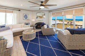 Ein Wohnzimmer mit großem Fenster, Deckenventilator und Blick auf den Strand.