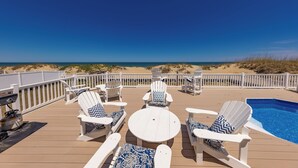 A deck with white Adirondack chairs, a round table, and a pool. - Seas the Moment - 4 BR Oceanfront with Pool (Virginia Beach)