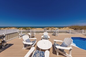 Eine Terrasse mit weißen Adirondack-Stühlen, einem runden Tisch und einem Pool.