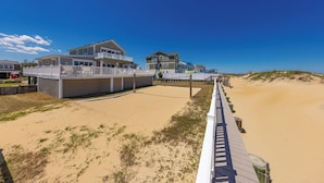 A beachfront property with a wooden boardwalk leading to a sandy beach, featuring multiple houses with balconies. - Seas the Moment - 4 BR Oceanfront with Pool (Virginia Beach)