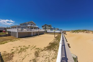 Ein Strandgrundstück mit einer Holzpromenade, die zu einem Sandstrand führt, mit mehreren Häusern mit Balkonen.