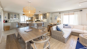 A spacious living area with a wooden dining table, wicker chairs, and a white sofa. - Seas the Moment - 4 BR Oceanfront with Pool (Virginia Beach)