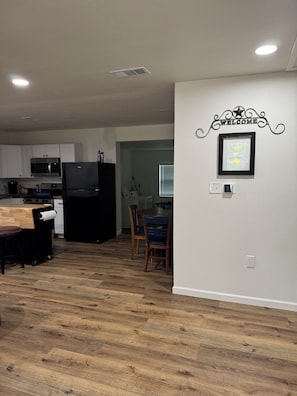 A kitchen with white cabinets, a black refrigerator, and a wooden dining table with chairs.