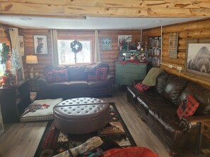 A cozy cabin-style living room with a fireplace, leather sofas, a coffee table, and a bookshelf. - Peaceful 2 bedroom cabin 4 Miles from Red Lodge perfect for relaxing getaways. (Roberts)