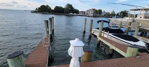 Ein Steg mit Booten, eine Holzpier und eine entfernte Küstenlinie mit Gebäuden.