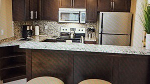 A kitchen with dark cabinets, a microwave, a stove, a refrigerator, and two stools.