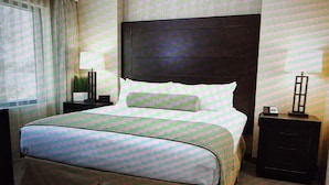 A hotel room with a large bed, a nightstand with a lamp, a dresser, and a window with curtains.