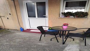 Un patio con una mesa redonda de vidrio, dos sillas negras y un jarrón de flores rosa.