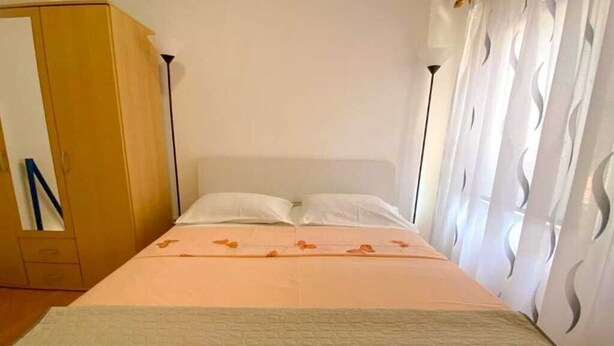 Una cama individual con una colcha blanca, un armario de madera y una cortina con un estampado ondulado.