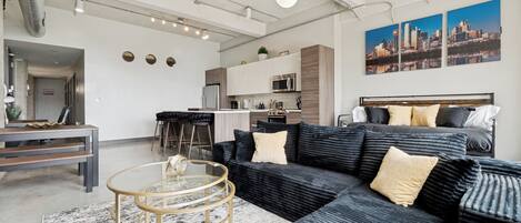 A modern living room with a sectional sofa, a glass coffee table, and a cityscape painting on the wall.