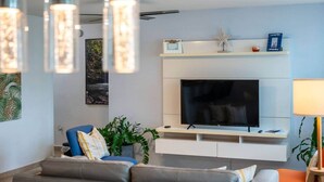 Ein modernes Wohnzimmer mit Flachbildfernseher, einer Couch, einem Couchtisch und Dekorationen auf einem Kaminvorsatz.
