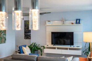 A modern living room with a flat-screen TV, a sofa, a coffee table, and decorative items on a mantel. - Hillside Village 3BR Oasis w/ Private Terrace (Mameyes II)