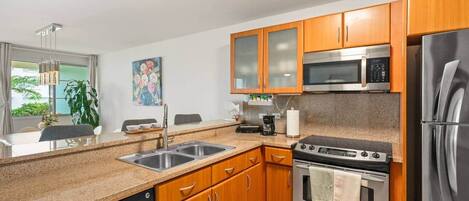 A modern kitchen with granite countertops, stainless steel appliances, wooden cabinets, and a window with a view.