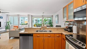 Eine moderne Küche mit Holzausstattung, einem Geschirrspüler, einem Herd und einem großen Fenster mit Blick auf einen Balkon.