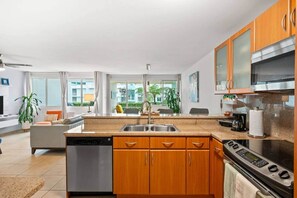 A modern kitchen with wooden cabinets, a dishwasher, a stove, and a large window overlooking a balcony. - Hillside Village 3BR Oasis w/ Private Terrace (Mameyes II)