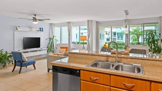 Eine moderne Küche mit Geschirrspüler, ein Essbereich mit Tisch und Stühlen, ein Fernseher und große Fenster mit Blick auf Grünfläche.