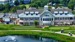 A golf course with a pond, a clubhouse with multiple windows, and a parking area. - Private Resort Retreat Near Rehoboth Beach in Exclusive "The Peninsula" (Millsboro)