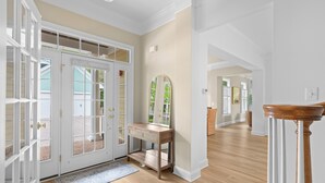 A hallway with a wooden floor, a white door with glass panels, a wooden console table with drawers, and a mirror. - Private Resort Retreat Near Rehoboth Beach in Exclusive "The Peninsula" (Millsboro)