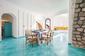Un comedor con una mesa dispuesta para cuatro personas, una pared de piedra y vista al cielo a través de una ventana.