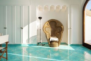 Una habitación con una gran silla de mimbre decorada, una lámpara de pie trípode y vistas a través de un ventanal arqueado.