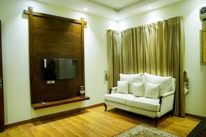 A living room with a sofa, a mounted TV, curtains, and a wooden floor. - Spacious 5BR, 2 kanal Luxury Family Home (Lahore)