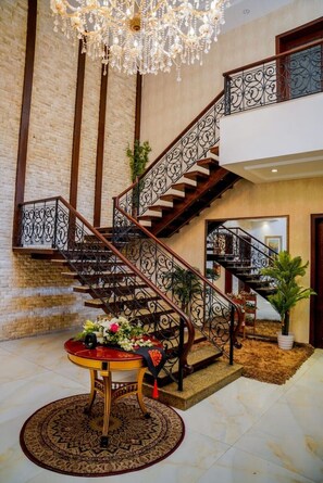 Un magnifique escalier orné de balustrades travaillées, un lustre et une table ronde décorée de fleurs.