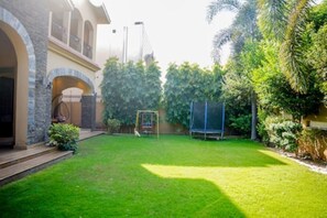 A well-maintained backyard with a lawn, a swing set, and a trampoline.