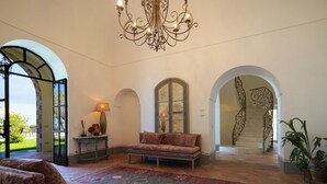 Ein geräumiger Innenraum mit einer Couch, einem gemusterten Teppich, einer Chandelüster und einer Treppe.
