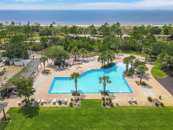 A swimming pool with a curved edge, surrounded by palm trees and lounge chairs.